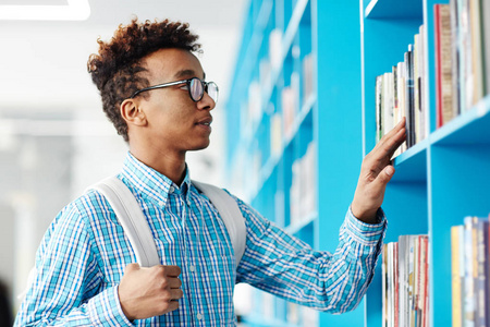 年轻的大学生站在书架上, 寻找下一课要读的书。
