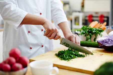 厨师在厨房做饭时, 用锋利的专业刀在木板上切割绿色植物