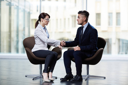 企业家握手自信的企业家与长黑发握手她的商业伙伴, 而他们坐在对方