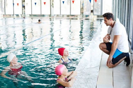 运动训练中的年轻游泳教练与成熟女性在泳池中交谈