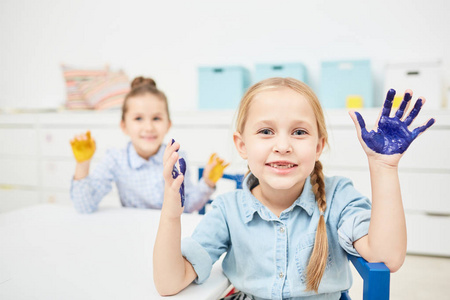可爱的孩子, 她的手掌在蓝色的油漆看相机在幼儿园或小学的课程