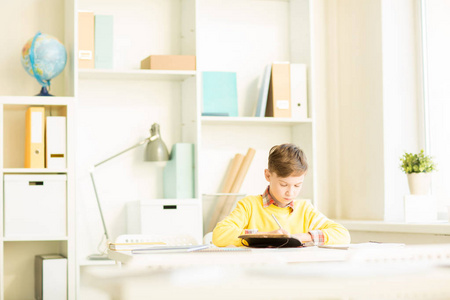 可爱的小男孩做笔记或 wiriting 在家中作业在笔记本上, 而坐在办公桌旁