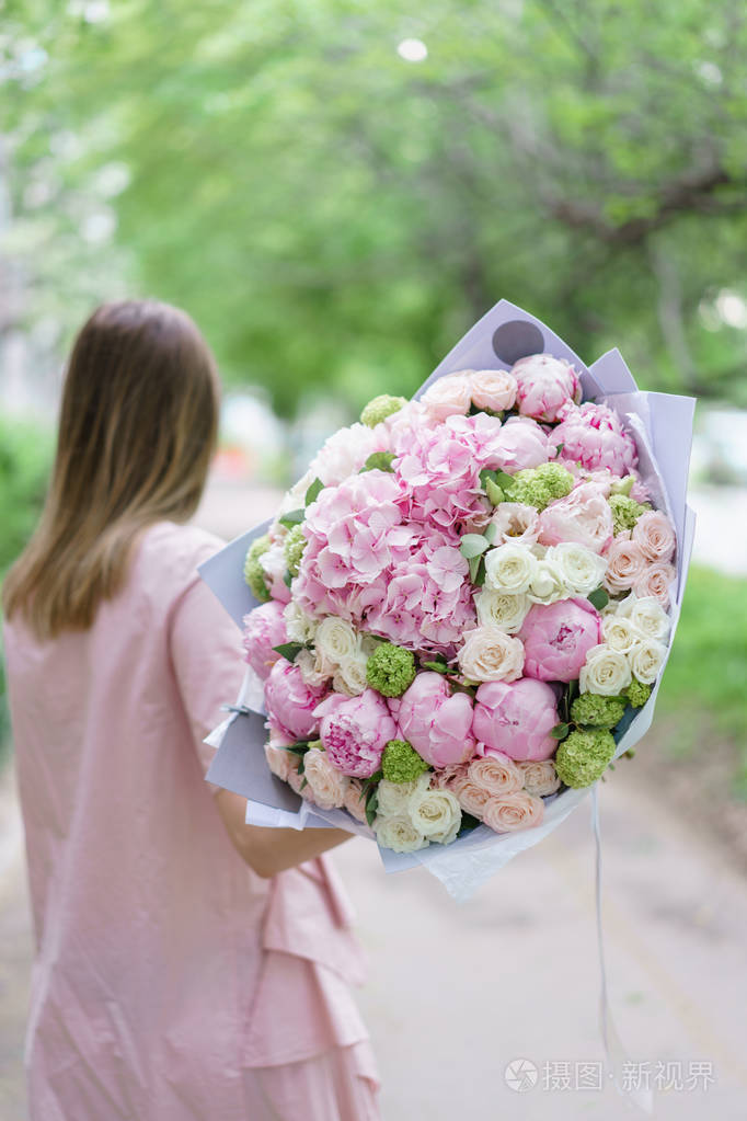 年轻女孩捧着一束美丽的春天花束.花的安排与绣球和牡丹.颜色浅粉色.