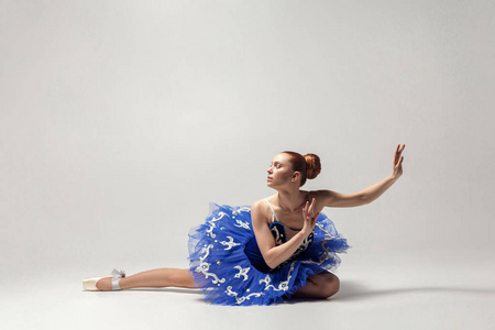 迷人的芭蕾舞演员在蓝色礼服优雅地坐在白色工作室地板上