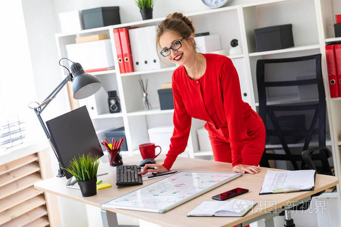 一个年轻的女孩站在办公桌旁的办公室, 并与计算机, 标记和磁板工作