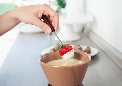 妇女浸泡成熟的草莓到碗中的白色巧克力火锅桌上