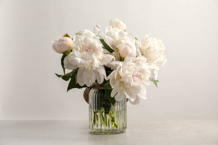 花瓶与美丽盛开的牡丹在桌子上反对光背景