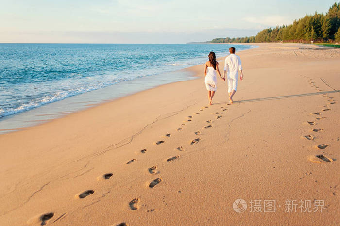 后视图的相爱的双方留有脚印在沙滩走走
