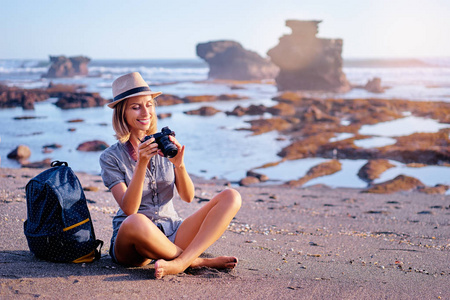 美丽的年轻女子与相机和背包在海洋海滩