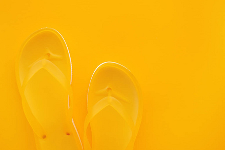 与复制空间相同的颜色背景下的黄色翻转触发器对的顶部视图。沙滩凉鞋或拖鞋在简约温暖的夏天色调的成分