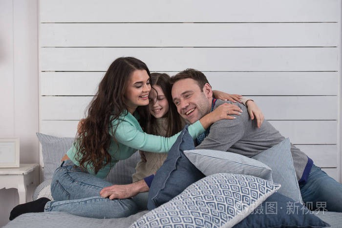 家庭的幸福父母和女儿在床上拥抱的肖像