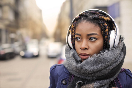黑色非洲妇女与耳机听音乐在街上的冬天