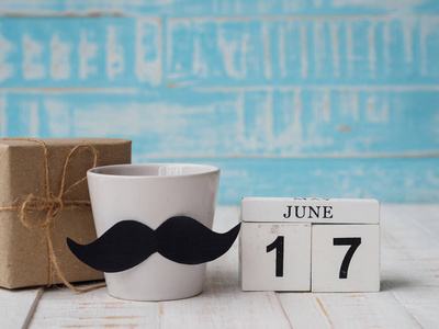 父亲节快乐的概念。6月17日木块日历, 礼品盒, 一杯咖啡与胡子在蓝色木质背景