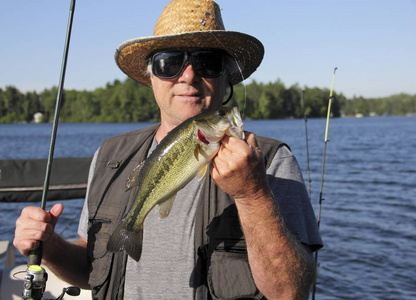 渔夫拿着一个蓝色的天空和湖作为背景的大嘴低音照片