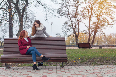 在秋季城市公园的长凳上, 两个快乐可爱的美丽少女