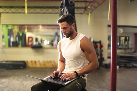 私人教练坐在他的笔记本电脑在健身房工作