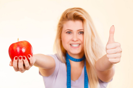 饮食减肥, 健康食品, 水果概念。金发女人与测量磁带周围的脖子持有大红苹果显示拇指向上的手势