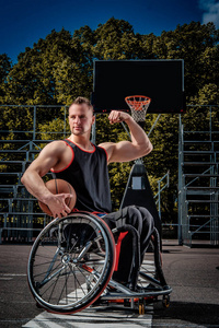 强大的篮球运动员在轮椅上的姿势与球在开放的游戏场地