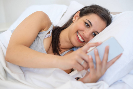 快乐的女人看智能手机显示在床上