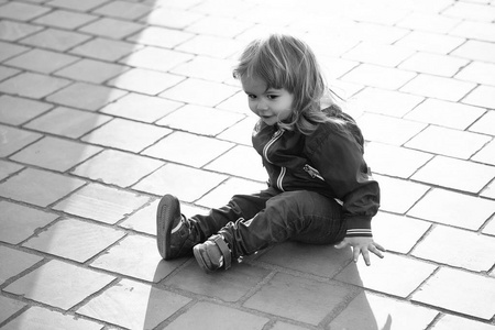 孩子正坐在柏油上。小男孩坐在人行道上