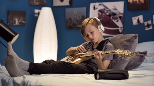 男孩在耳机学习歌曲与吉他图片