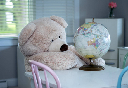 一只巨型泰迪熊看着玩具地球仪, 也许在寻找一个新的地方度假。