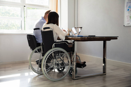残疾女商人坐在她的伙伴与膝上型电脑办公桌在办公室