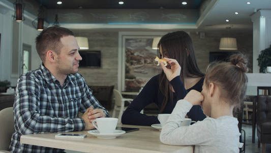 团圆的幸福的家庭，在咖啡馆里。父亲 母亲和女儿微笑和在一起聊天