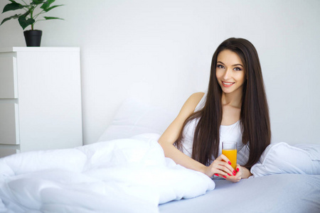 性格开朗的女人喝橙汁，坐在她家里的床上