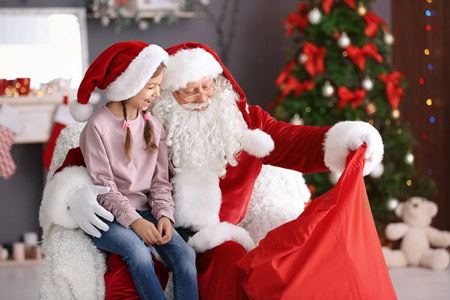 真实的圣诞老人显示他的袋子与礼物对小女孩室内