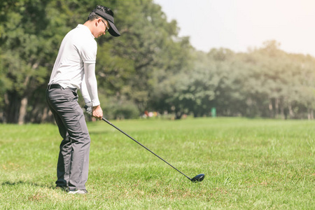 亚洲男人打高尔夫球。男子站在球场上打高尔夫球