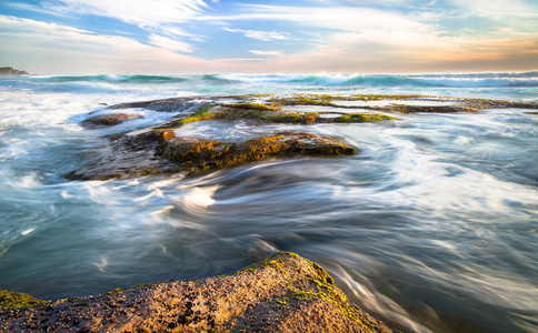 在澳大利亚维多利亚大奥特韦国家公园乔安娜海滩上日落时, 海浪在岩石 tidepools 上的长时间曝光