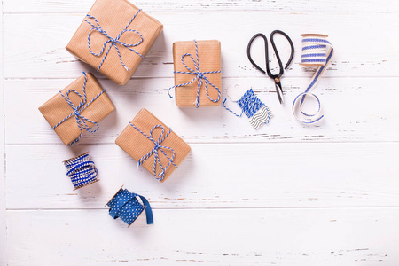 节日礼品盒与礼物, 剪刀, 蓝色丝带和标签在纹理的木质背景。选择性对焦。文本的位置。平躺