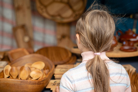 这个女孩正在看市场上的木制品。从后面查看