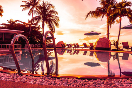 美丽的户外景观与雨伞和椅子周围的游泳池在豪华酒店和度假村在日出时的旅行和度假