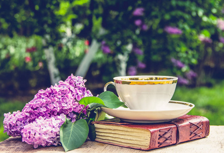 书, 杯茶和丁香花.香茶在花园里.浪漫的概念.复古随身携带照片