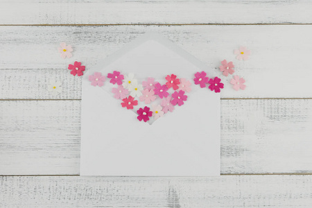 白色信封装饰与粉红色的纸花在白色的木材背景