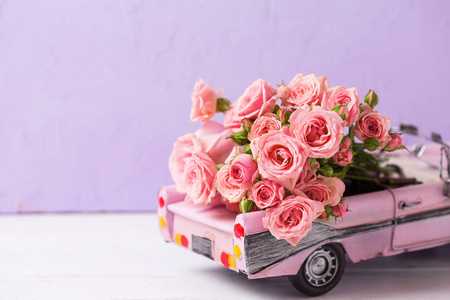 复古汽车玩具与粉红色玫瑰花反对紫色纹理墙。浪漫的背景。选择性对焦。文本位置