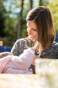 微笑的母亲母乳喂养她的小女孩, 因为他们坐在一起, 在花园的桌子上