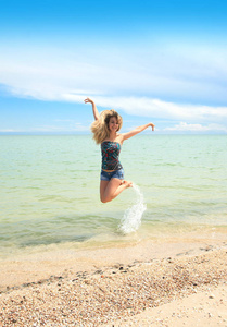 一个美丽的女人愉快地跳在沙滩上, 在炎热的阳光明媚的一天