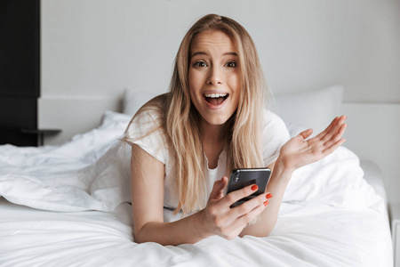 照片中的可爱兴奋美丽的年轻女子在家中使用手机聊天.