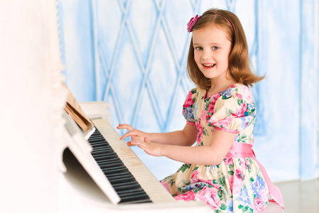 穿着白色连衣裙的小女孩弹钢琴。音乐和艺术概念。音乐学院