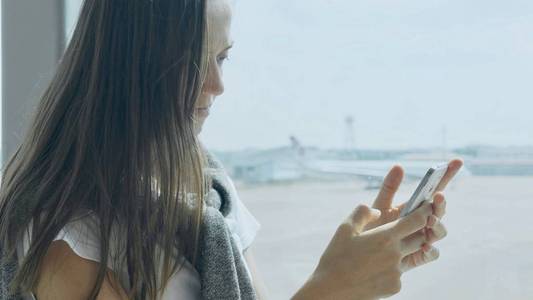 年轻女子使用智能手机在机场与飞机的背景