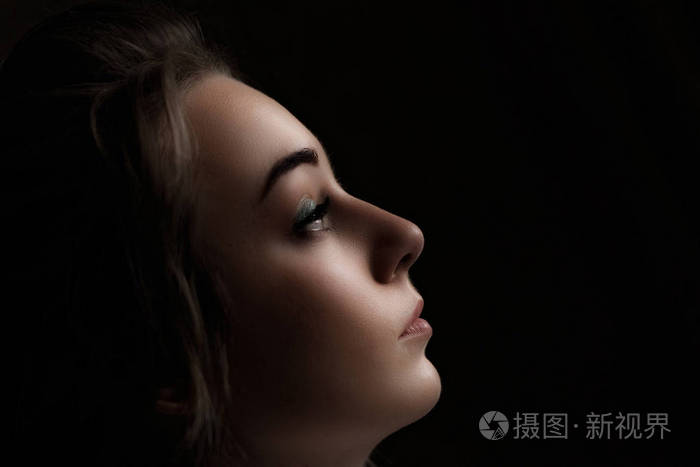 美丽女孩的脸被黑色背景所孤立.黑色背景上女性脸的剪影.侧面视图