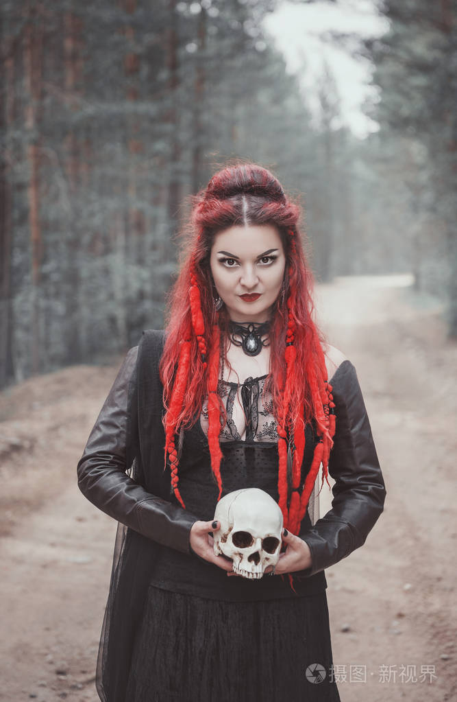 美丽的妇女巫婆与红色头发和头骨在手在森林室外照片-正版商用图片0