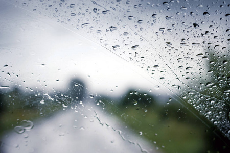 在旅游线路上行驶时, 汽车的湿挡风玻璃。汽车玻璃上滴下的雨滴。通过公共汽车的湿玻璃可以看见的路