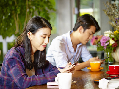 两位年轻的亚洲成年人坐在咖啡馆里玩手机的男人和女人照片