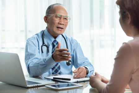 亚洲高级男医生与女性病人在一间医疗室谈蓝衫