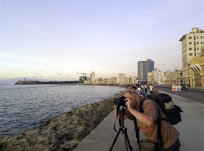 摄影师与照相机在日落期间与大西洋, 住宅大厦和莫洛城堡在背景马雷贡海滨大道, 哈瓦那, 古巴