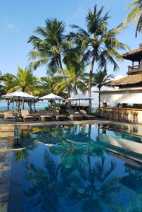 在印度尼西亚巴厘岛的海滩度假胜地, 棕榈树环绕着游泳池和酒吧设施, 用于旅行背景